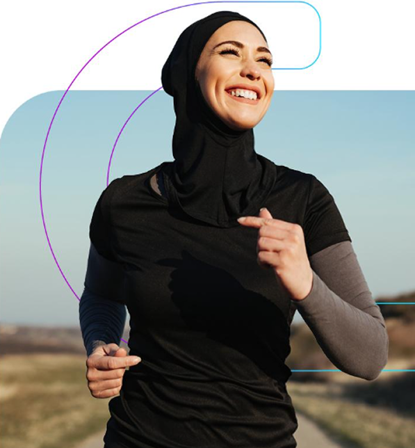 Smiling young woman wearing a sports hijab jogging along an open path under clear skies, symbolizing active healthy living.